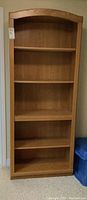 Front view of the faux wood bookcase showing five shelves with a curved top edge.