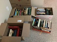Photo of four cardboard boxes filled with hardcover books viewed from above, showing a variety of book sizes and colors.