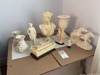 Overview of the lot showing various decorative busts, statuettes, vases, and figurines arranged on cardboard surface.