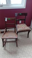 Side-by-side image of two wooden chairs against a maroon wall, showing the rocking chair and needlepoint seat chair.