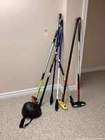 Four curling brooms leaning against wall with black helmet on floor