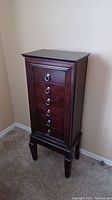 Front view of tall dark wood jewelry armoire with six drawers and ring pulls