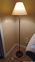 Full view of the metal look floor lamp standing in a corner with lampshade illuminated.