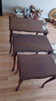 Three solid wood nesting tables shown stacked, highlighting size difference and scalloped wooden edges.
