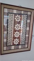 Framed tapa cloth showing traditional floral and geometric designs in earthy tones.