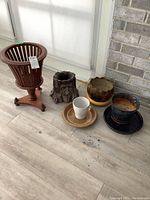 Photo showing all items in the lot including wooden plant stand, resin planter, ceramic planters, and saucers on light wood flooring