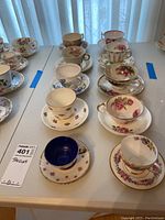 Overview of all 10 vintage teacups and matching saucers on a white table with floral and decorative motifs