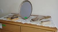 Full view of all vanity set items arranged on a dresser, showing the oval mirror standing upright and multiple brushes spread out.