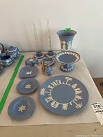 Full table view of Wedgwood jasperware collection showing two candleholders with clear glass candles, teapot set, small trinket box, heart-shaped dish, perfume atomizer, plates, ashtrays, and footed dish arranged on table