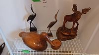 View of five wooden animal figurines on display including a large duck with round box, two egret birds, and moose sculpture showing overall condition