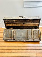 Open antique wooden carpenter's box showing internal compartments with various tool parts, mainly old Stanley plane components.