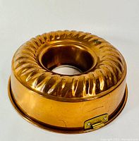 Side angled view of the antique copper bundt cake mould showing fluted exterior and metal clasp on the side.