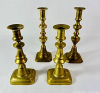 Front view of the four antique brass candlesticks showing two taller intricate and two shorter simpler designs