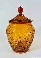 Front view of amber glass cookie jar with lid in place, showing floral embossed surface and knob on lid.