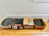 Four cardboard boxes of new nails arranged on floor showing nails and open box flaps.