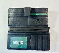 Interior view of black leather wallet showing card slots, ID window with Roots card, and embossed Roots logo.