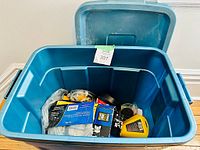 Rubbermaid Roughneck bin open with assorted painting supplies including cans, tapes, and tools inside