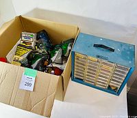 Box and metal organizer containing various HO scale tools and parts for model train scenery and maintenance.
