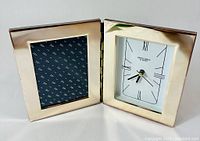 Front view of vintage silver-plated folding photo frame and clock set opened to show clock face and photo slot with decorative insert.