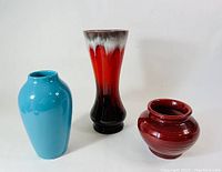 Photo showing three pottery vases together: tall oxblood vase with black and white drip, rounded oxblood vase, and bright blue vase.