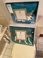 Two sealed Angel Wrap and Sock sets stacked, showing teal blankets with socks inside clear packaging and ribbons.