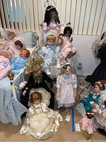 Overall grouping of six collector's dolls seated and standing, dressed in period and fantasy clothing, accompanied by doll furniture.