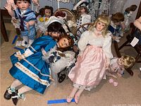 Wide shot showing multiple heirloom quality collectible dolls in varied clothing and sizes arranged on floor and furniture, displaying their detailed features and costumes.
