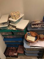 Stacked plastic storage containers, baskets, and a heart-shaped box filled with various crafting supplies