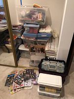 Multiple containers stacked in a corner filled with various crafting supplies including plastic boxes and gift boxes