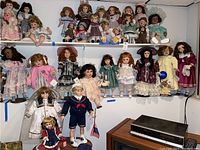 Wide view showing most of the 12 dolls arranged on shelves, showcasing a variety of period clothing styles and accessories.