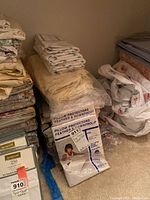 Multiple folded king size sheets and pillow protectors stacked on floor of room.