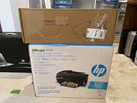 Two stacked boxes; lower box is HP Officejet 4630 printer, upper box is HP QL122 laminator.