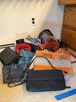 Photo showing assorted women's purses arranged on carpet, includes various sizes, colors, and materials.