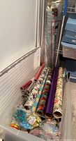 Side view of plastic bin holding multiple rolls of gift wrap and bags with ribbon bows.