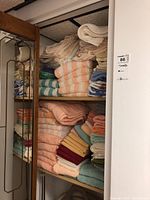 Wooden closet shelves holding stacks of folded bath towels and washcloths in white, cream, peach, green, striped and patterned designs