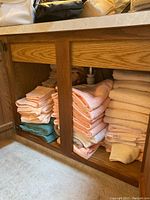 Stacked bath towels in peach, turquoise, and beige colors stored in an oak cabinet under a counter