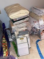 Stack of folded sheets and pillow cases arranged against a wall on carpeted floor.