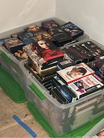 Photo of one plastic tote filled with multiple VHS tapes showing front covers of various movies from different genres.