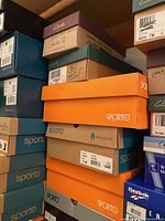 Stacked shoe boxes from brands Clarks, Sporto, Reebok, and others showing multiple women's shoes and boots.