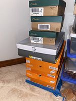 Stack of shoeboxes including three Clarks boxes labeled bone and navy, multiple Sporto boxes, and other assorted shoe boxes.