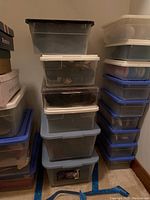 Six plastic totes stacked containing women's boots, shoes, and sandals.