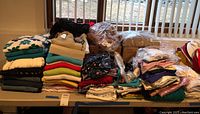 Wide view of various folded women's clothing items on a table, including sweaters, tops, and packaged garments.