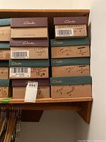 Stacked shoe boxes labeled with Clarks brand and handwritten tags indicating sandal color and size.