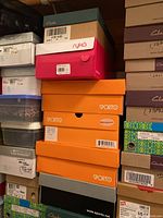 Stack of shoe boxes from brands including Sporto (orange), Clarks (green and brown), Ryka (pink and white)