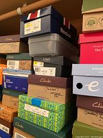 Stack of various shoe boxes mostly Clarks and Chaps including a blue Reebok box on top.