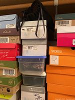 Stacked shoe boxes and plastic containers with multiple brands including Clarks and Sporto, labeled with sizes 7 and 7.5, and colors such as black, gray, silver