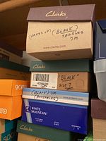 Stacked shoeboxes from various brands including Clarks, White Mountain, Pure Sole, Reebok, and Moda. Boxes labeled with shoe types, colors, and sizes.