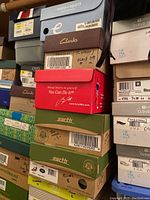 Stacked shoeboxes of various brands and sizes with visible labels and colors noted