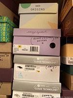 Stack of shoe boxes including Earth Origins, Easy Spirit, and Bzees brands with labels indicating shoe sizes 7 and 7.5 and colors like black and silver, navy, and green with flowers.