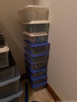 Nine clear and blue-lidded totes stacked containing various women's shoes.